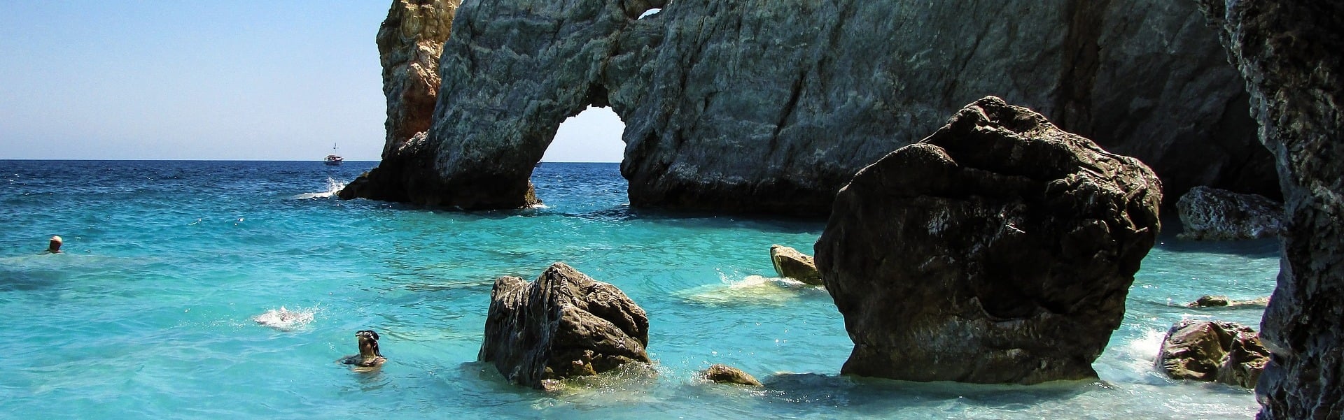 Skiathos yacht charter: swimmers in clear turquoise water beneath a rock arch on Skiathos