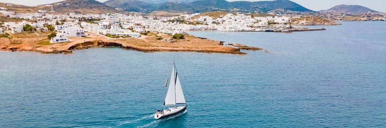 An AHOY yacht sailing towards a Cycladic island town