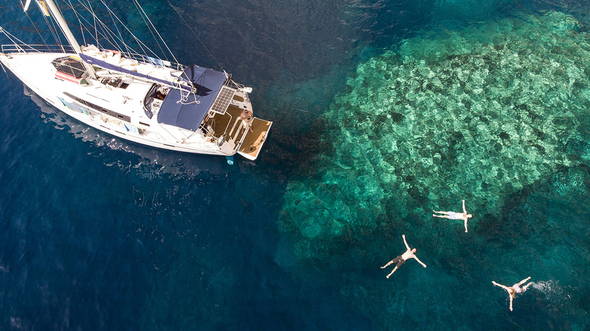 3 peple swimming off back of yacht