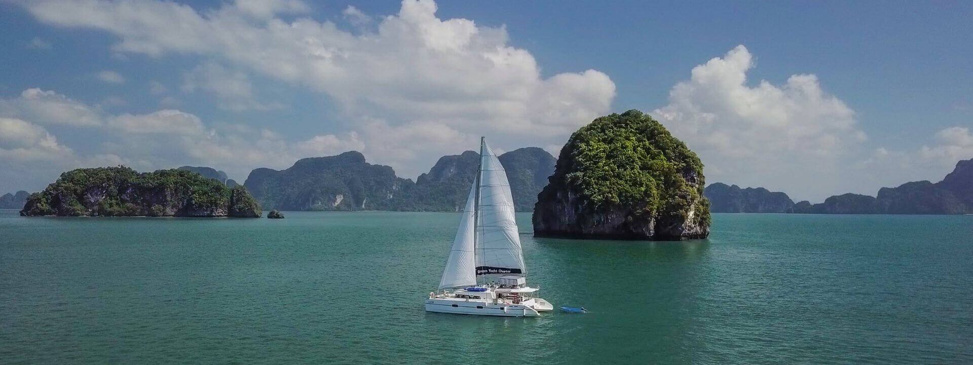 A sailing yacht cruising through calm green waters surrounded by lush islands, symbolising the essence of yacht charter preparation.