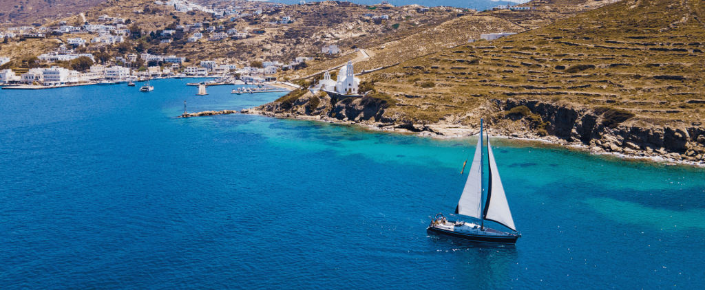 A sailing yacht navigating calm waters near a coastal village, reflecting the principles of practical yacht charter safety