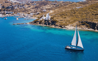 A sailing yacht navigating calm waters near a coastal village, reflecting the principles of practical yacht charter safety