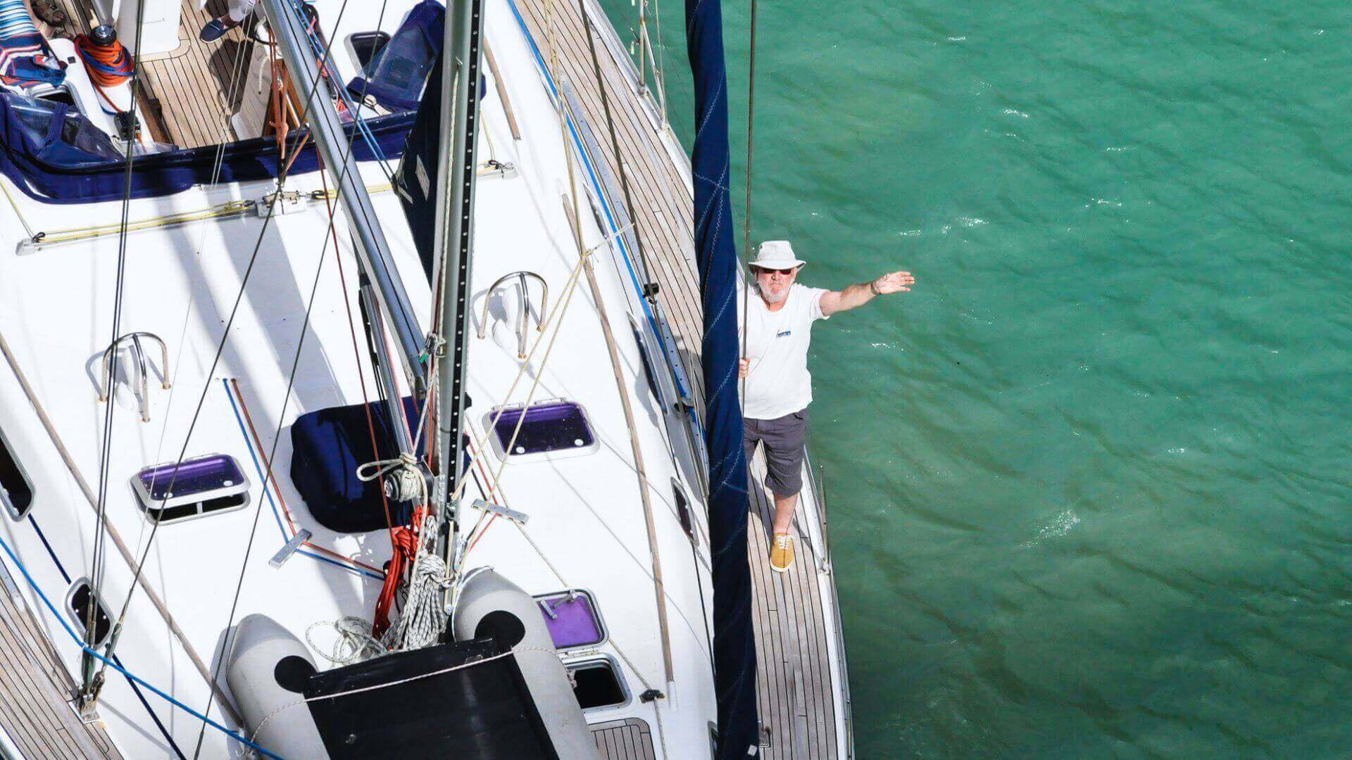 A skipper standing on the deck of a yacht docked in calm turquoise water, symbolising yacht charter preparation and safety.