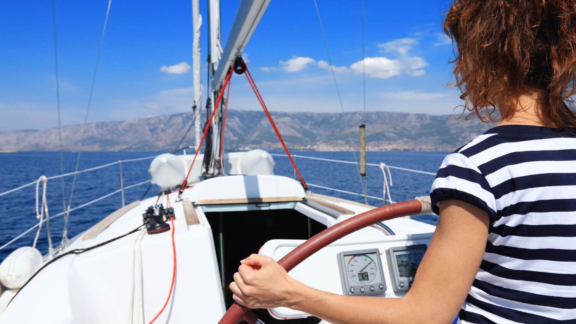 A woman steering a yacht with clear navigation equipment displayed, symbolising practical yacht charter tips for confident manoeuvring. 