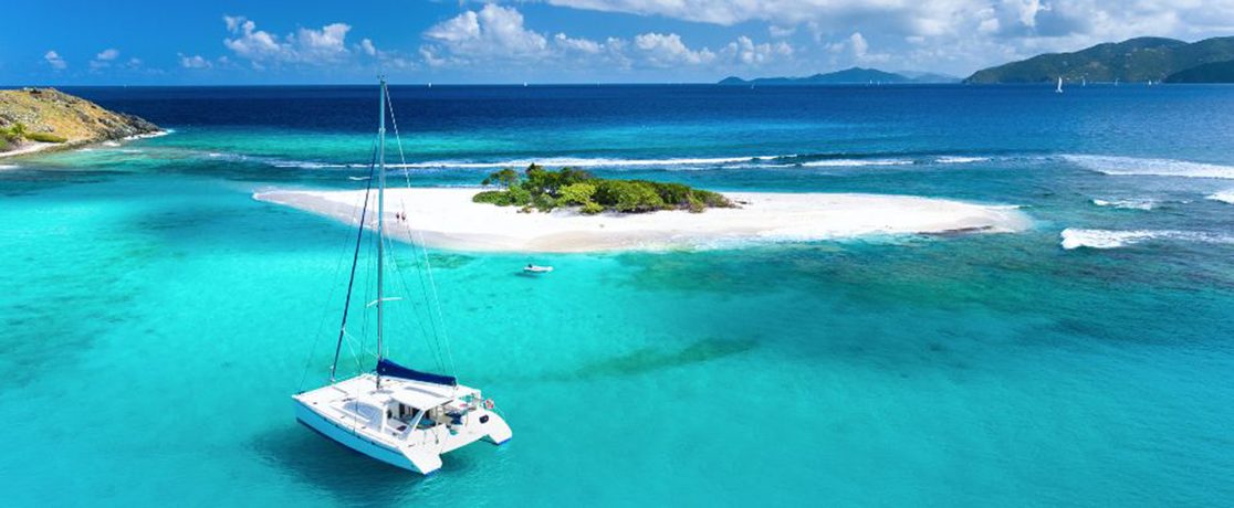 A catamaran anchored off a small sandy islet in the BVI