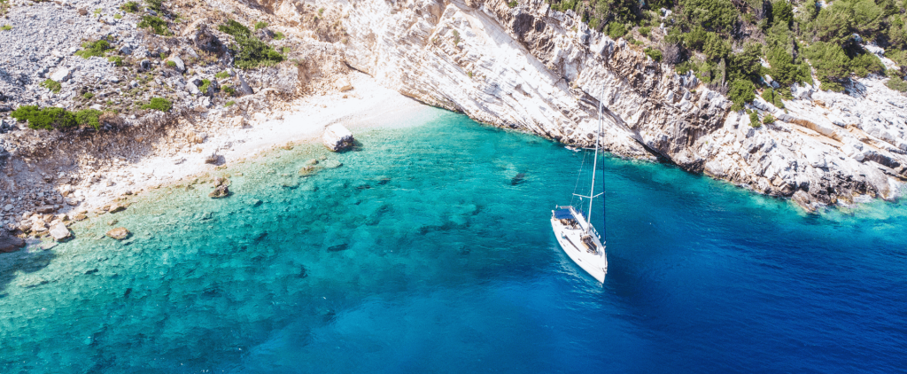 A yacht anchored near stunning rocky cliffs and clear blue water, highlighting the beauty of yacht charter preparation