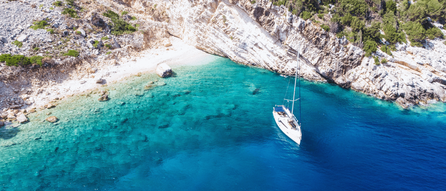 A yacht anchored near stunning rocky cliffs and clear blue water, highlighting the beauty of yacht charter preparation