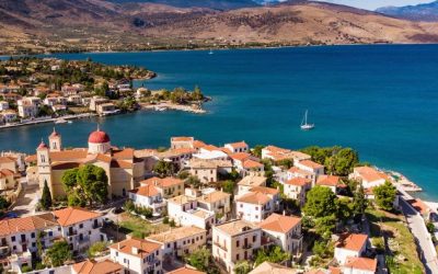 A stunning aerial view of the Saronic Gulf, showcasing a serene coastal village with red-roofed houses and clear blue waters, ideal for a sailing adventure.