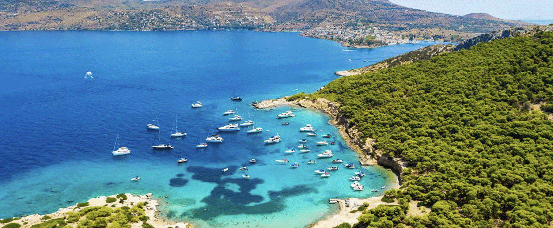 A stunning aerial view of yachts anchored near the lush green coastline of Aegina, a top island in Saronic Gulf.