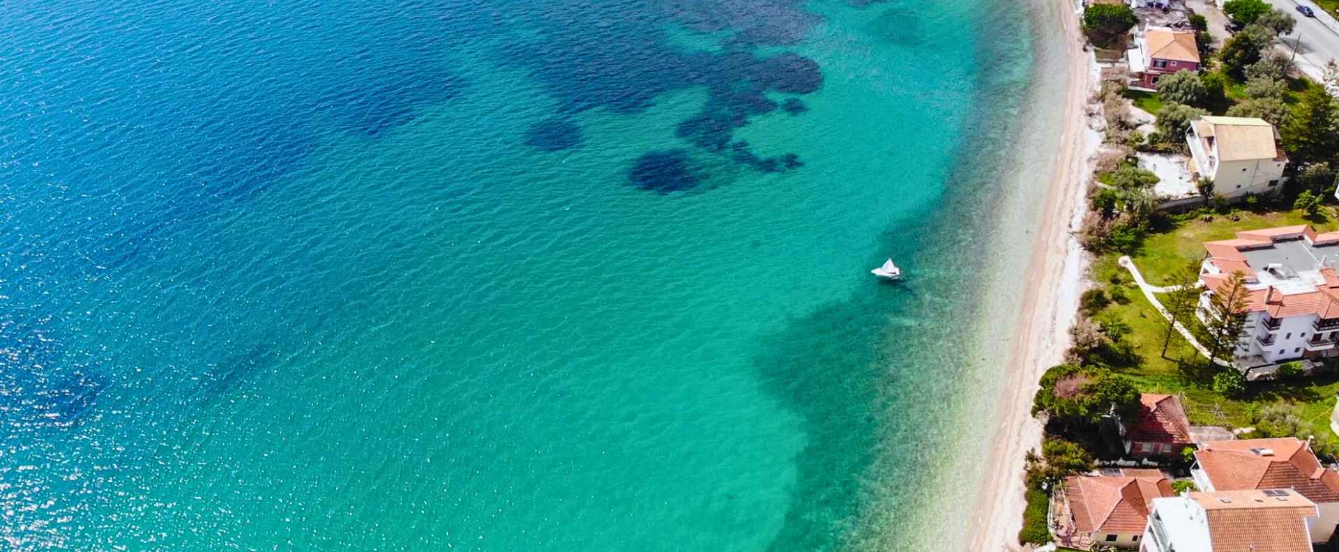 A small sailboat glides along a turquoise coastline, an ideal setting to learn to sail