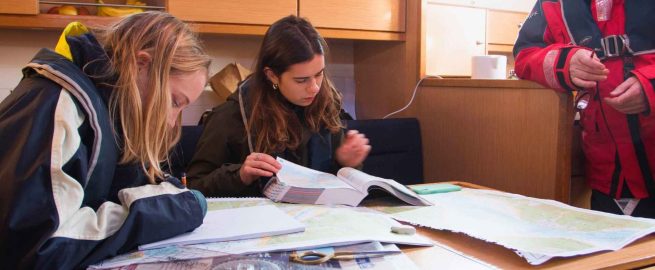 Two students working on navigation charts inside a yacht