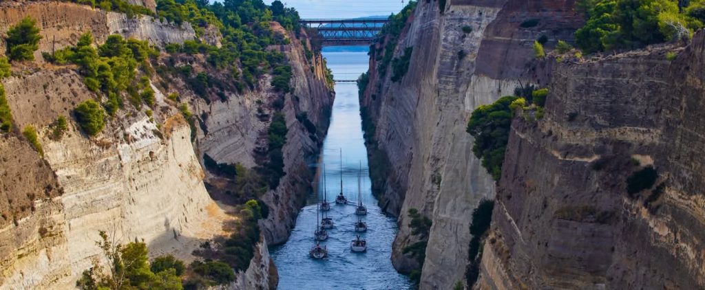 A flotilla passing through the Corinth Canal in Greece, surrounded by towering cliffs.