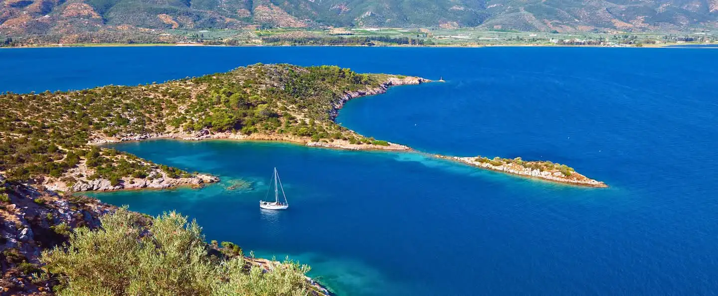 A yacht anchored in a secluded turquoise bay in Greece, surrounded by lush green hills