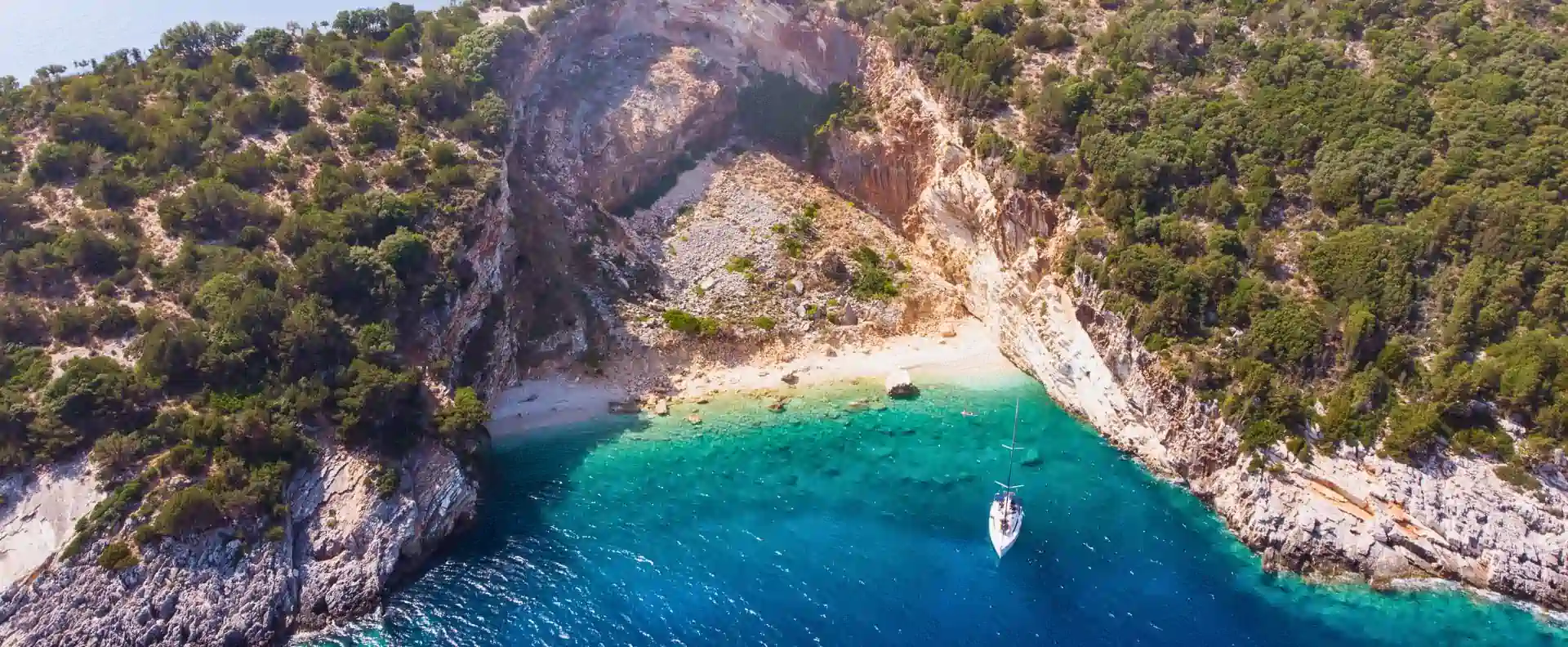 A yacht anchored in a remote bay surrounded by cliffs and pine forest in the Ionian Islands A yacht anchored in a remote bay surrounded by cliffs and pine forest in the Ionian Islands