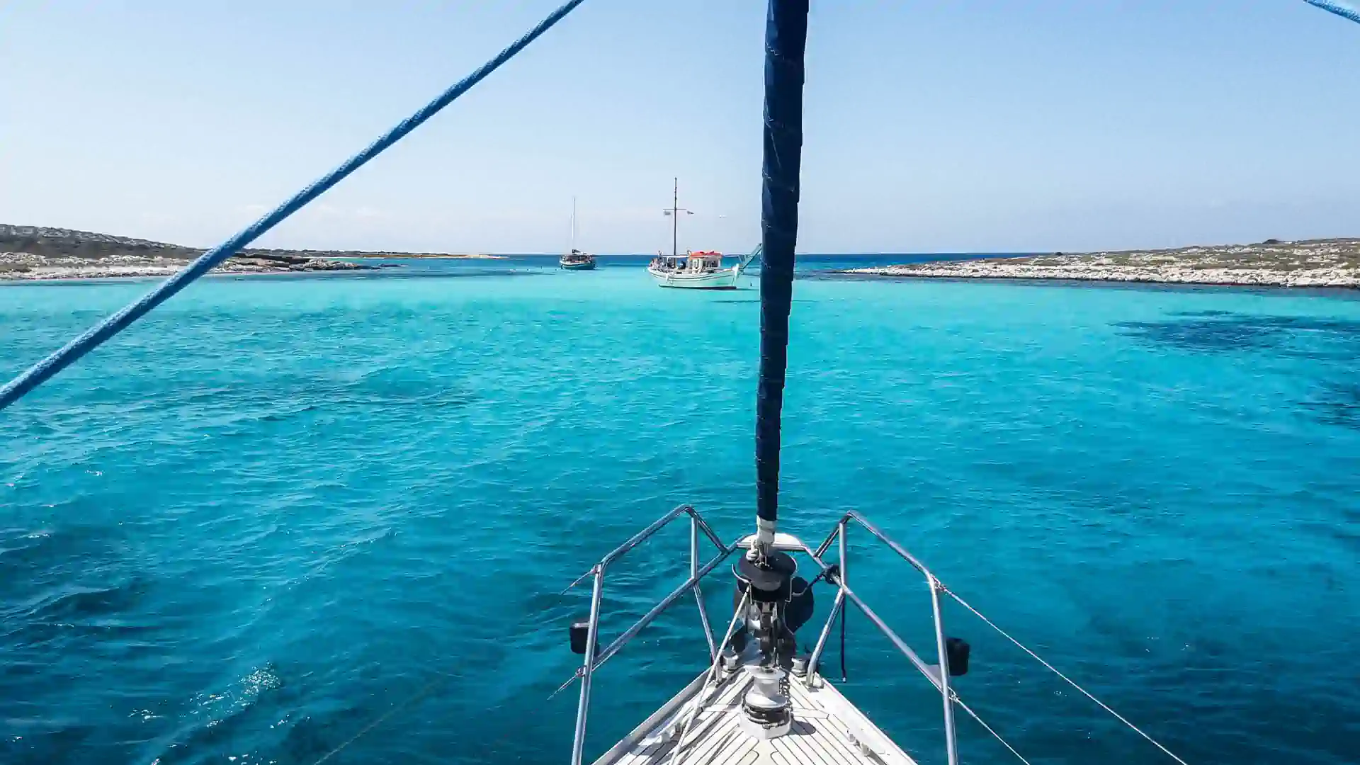 View from the bow of a yacht sailing through crystal-clear turquoise water in Greece