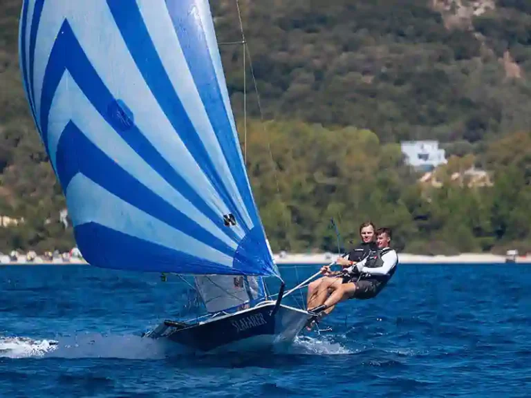 Two sailors flying a striped spinnaker on a dinghy off Nikiana