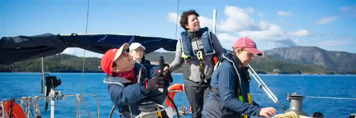 Sailing students participating in an RYA practical training session on deck, learning helming and winch techniques under instructor supervision in Greece