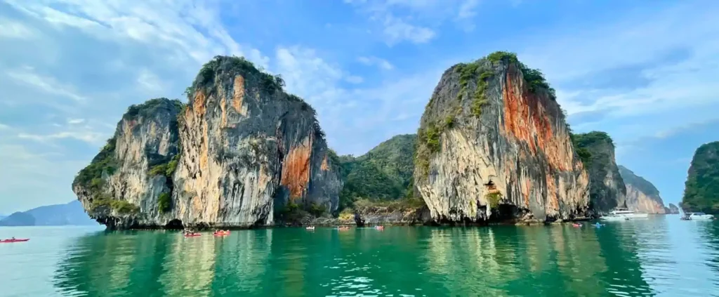 Kayakers glide beneath towering limestone karsts in Phang Nga Bay, Thailand.