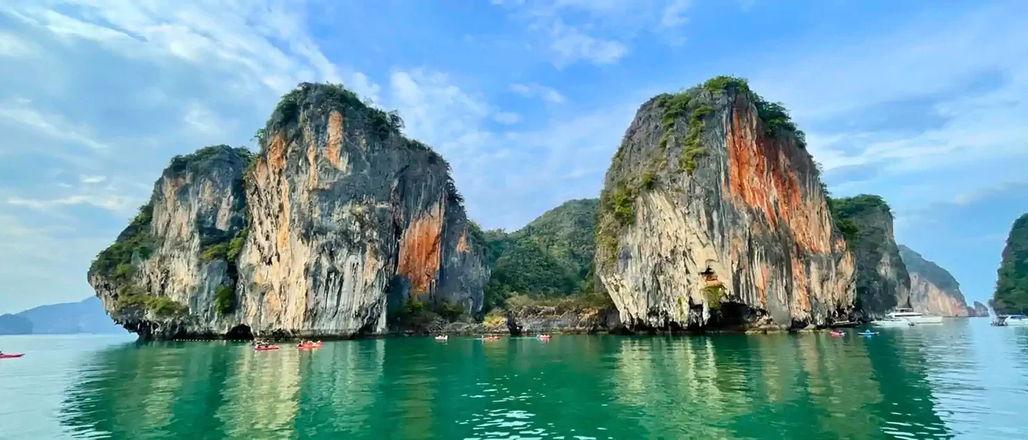 Kayakers glide beneath towering limestone karsts in Phang Nga Bay, Thailand.