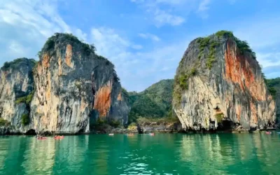 Kayakers glide beneath towering limestone karsts in Phang Nga Bay, Thailand.