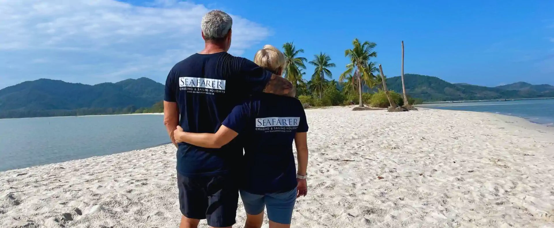 Seafarer flotilla skippers walking together along a palm-fringed white-sand beach in Thailand.