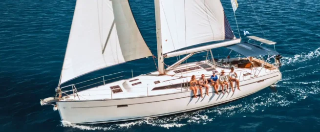 A monohull yacht sailing with guests on the rail, from above