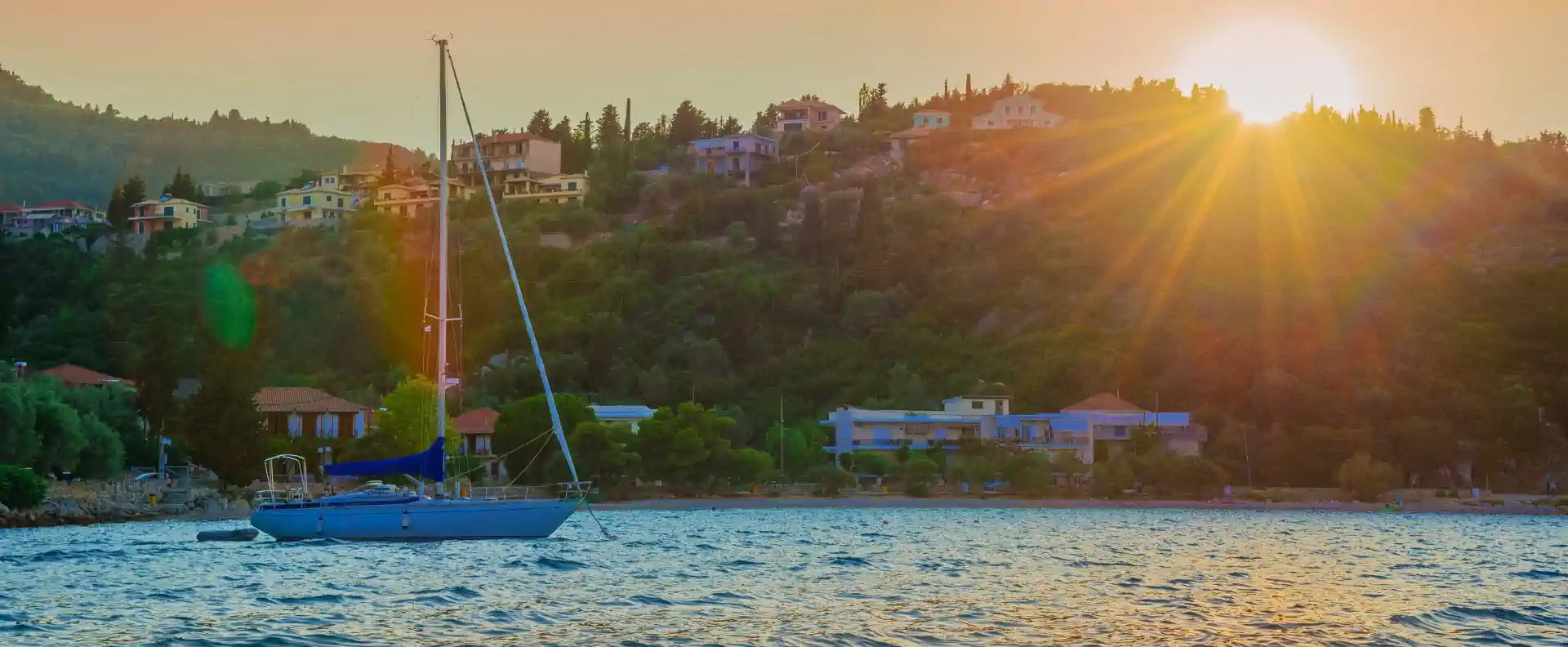 Sailing catamaran anchored at sunset near a Greek hillside village in the Ionian Sea.