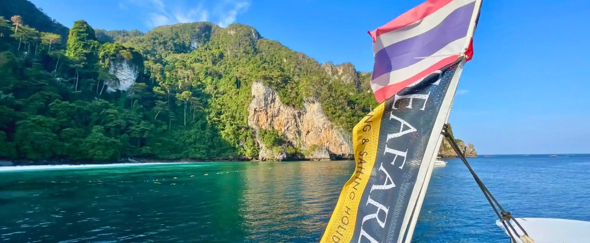 Thai flag and Seafarer banner on a catamaran sailing past jungle cliffs in Phang Nga Bay, Thailand