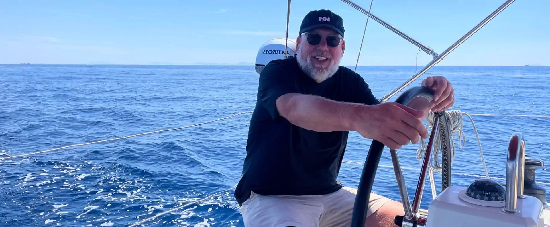Flotilla guest smiling at the helm during a Corinth Canal sailing holiday in Greece