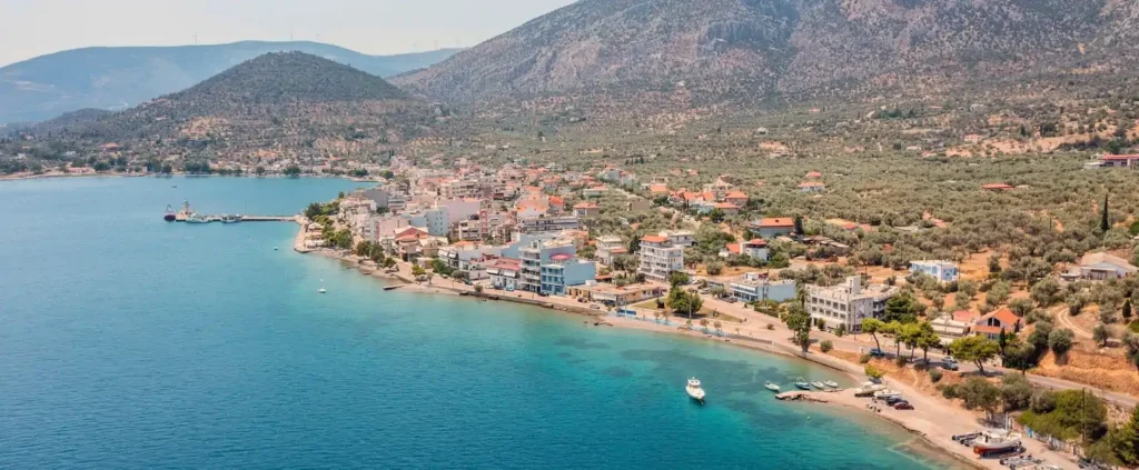 Aerial view of a coastal town on the Corinth Canal sailing route, surrounded by turquoise water and mountains