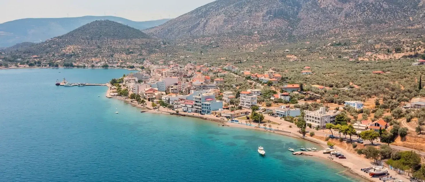 Aerial view of a coastal town on the Corinth Canal sailing route, surrounded by turquoise water and mountains