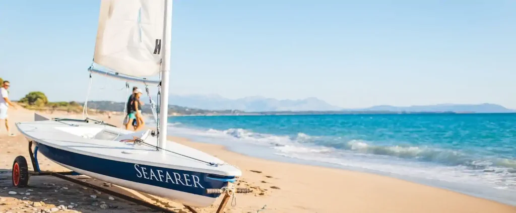 Seafarer sailing dinghy on the sand beside turquoise water, ready for beach club holidays at Poseidon