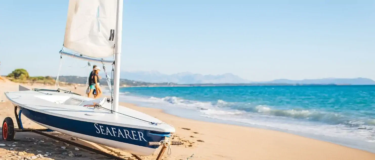 Seafarer sailing dinghy on the sand beside turquoise water, ready for beach club holidays at Poseidon