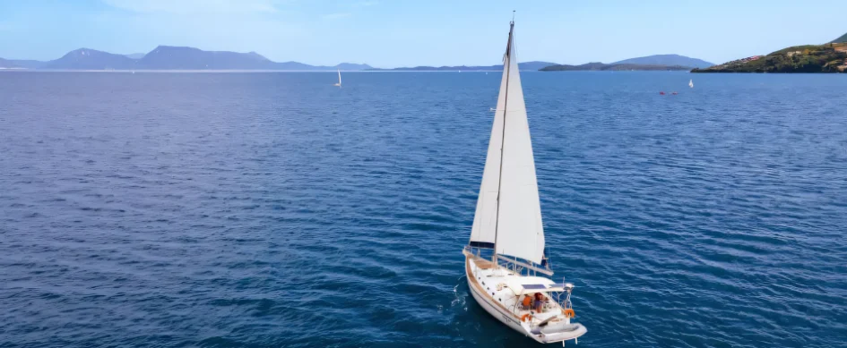 A Seafarer yacht under full sail on calm blue water in Greece, with islands on the horizon