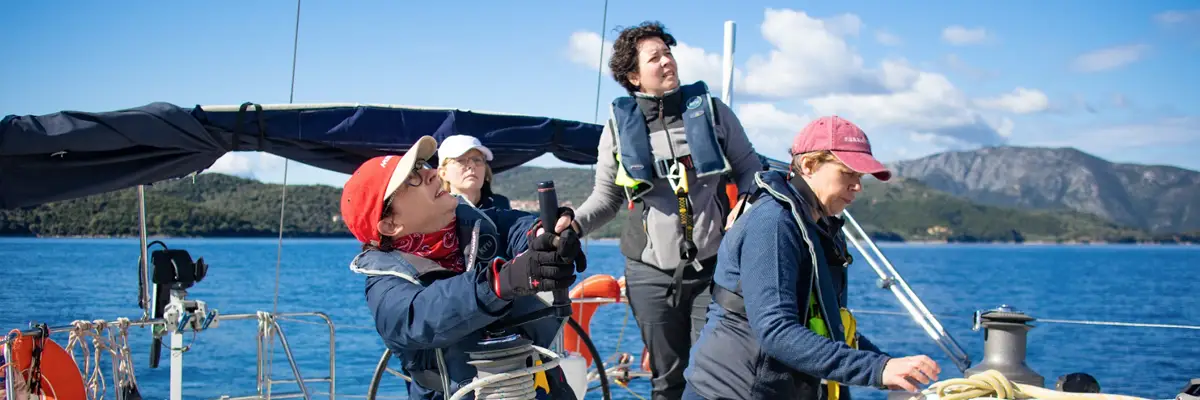 Four sailors in lifejackets trimming the sails on deck as they sail a yacht themselves