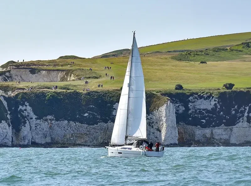 A yacht sailing past white chalk cliffs on the south coast of England, home of the Seafarer UK training centre
